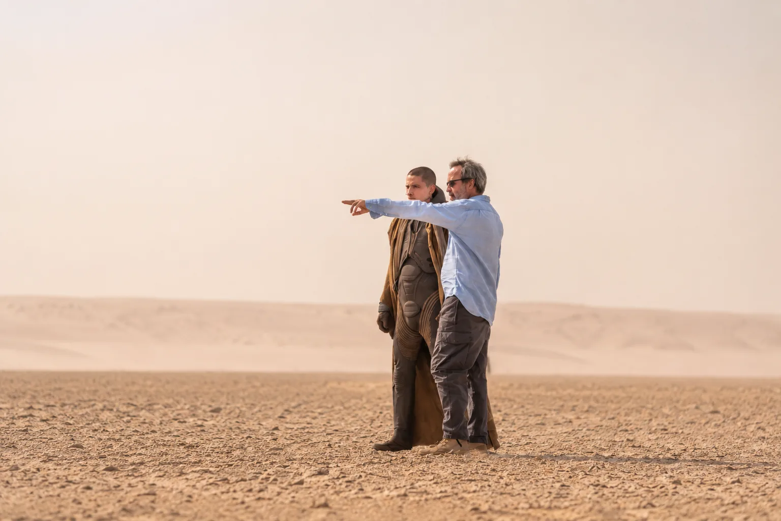 Behind-the-scenes view of a director and a cast member standing in the Abu Dhabi desert during the filming of Dune: Part Three.